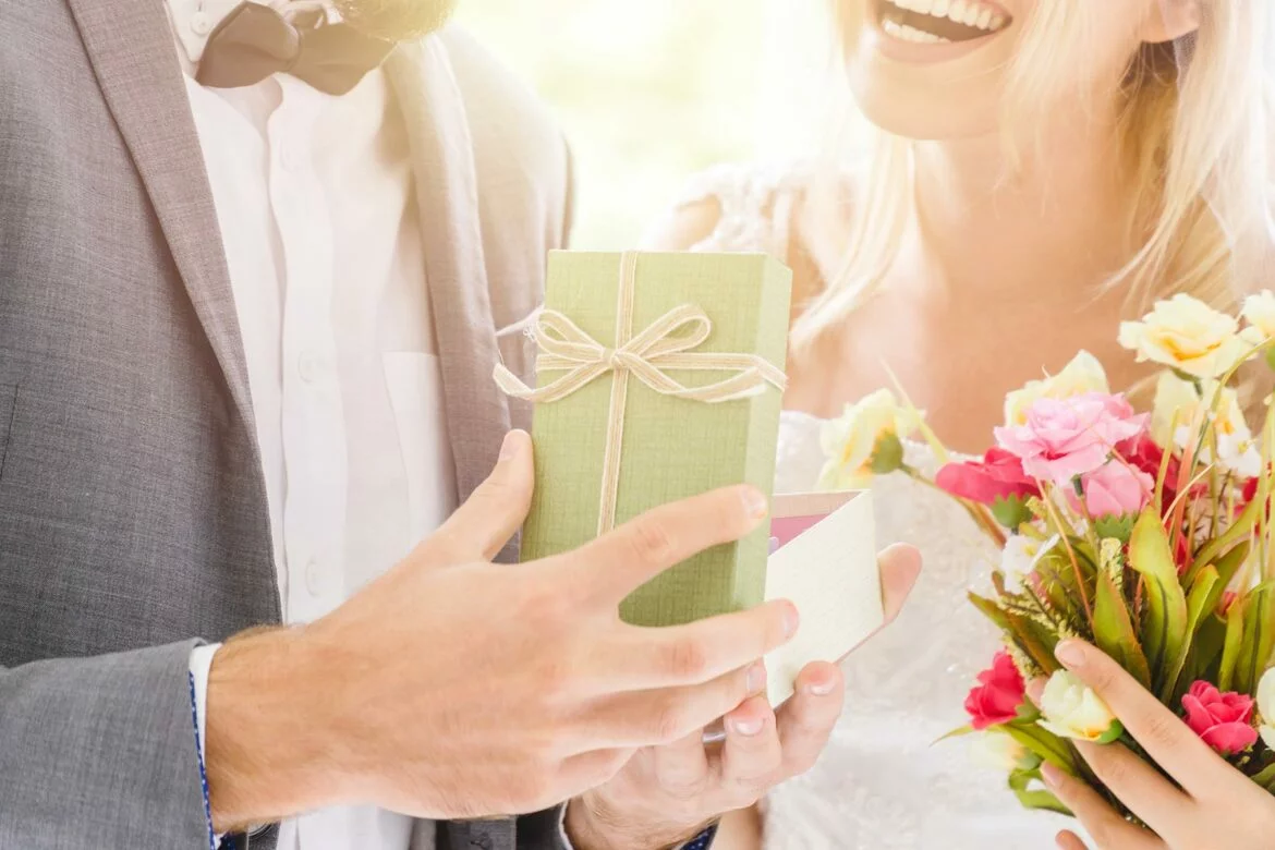 A groom holding an open box to show a bride during a wedding day gift exchange