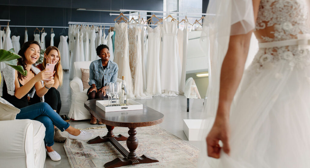 Group of three people sitting in a dress shop looking at a person in a wedding dress