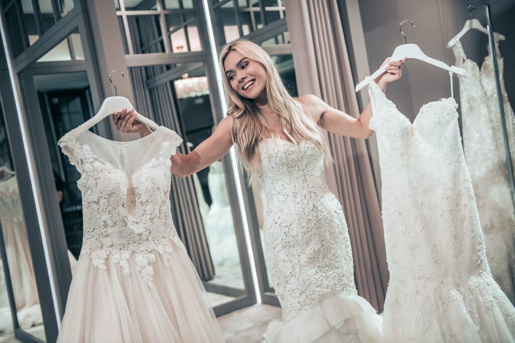 A woman in a wedding dress holding two other dresses on hangers