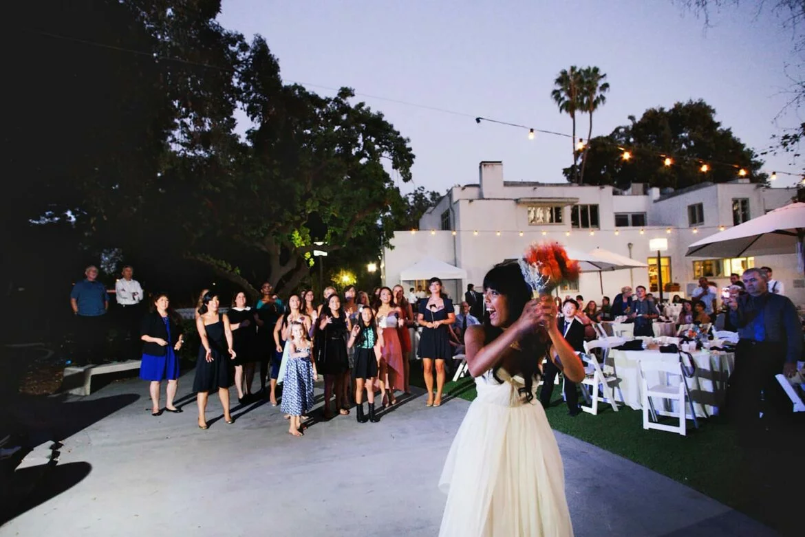 A woman wearing a wedding dress throwing a bouquet on the dance floor at a backyard wedding