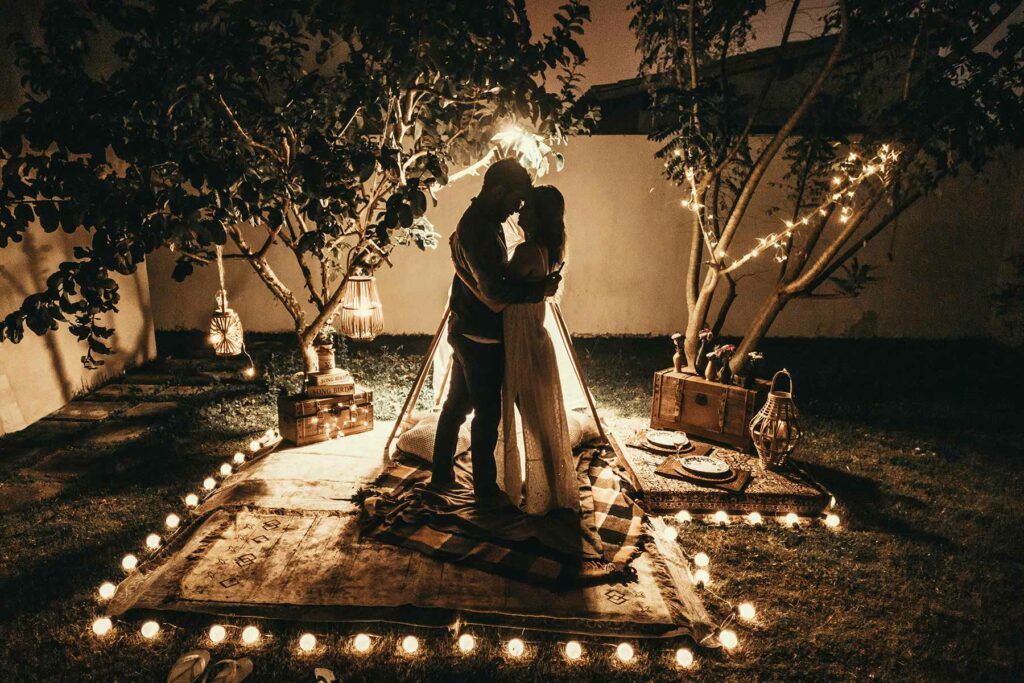 A couple in wedding attire embrace at an intimate backyard wedding surrounded by twinkling lights
