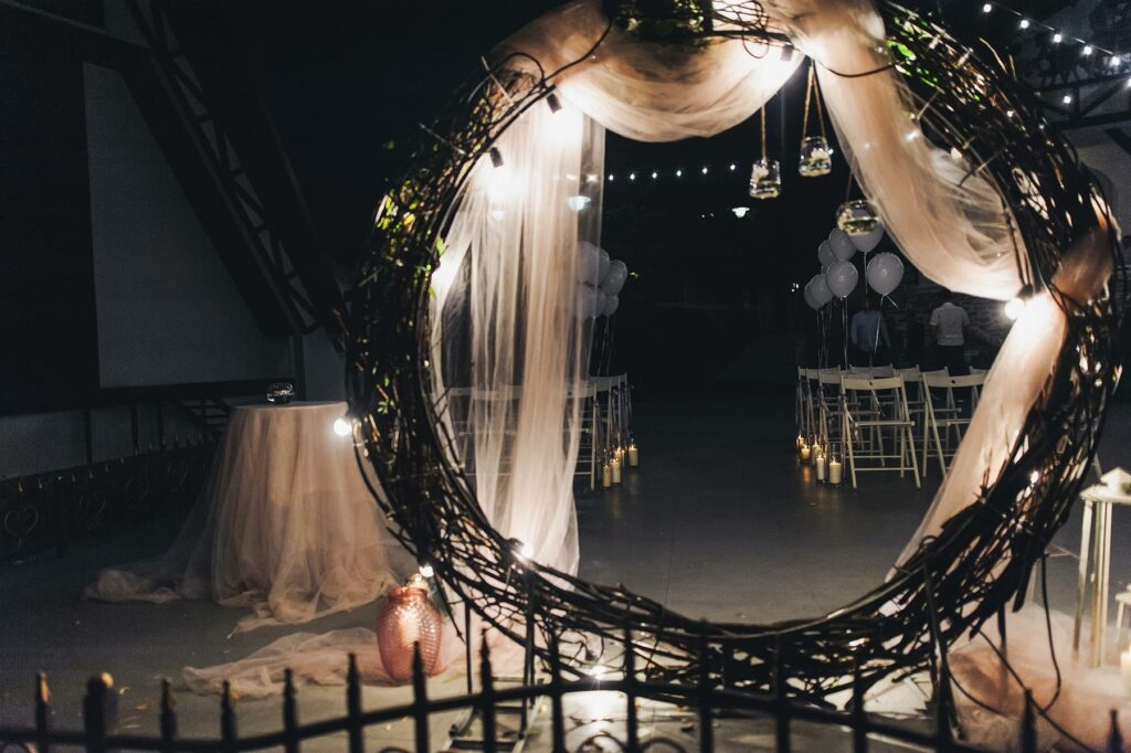 A decorative circular arch is draped in tulle and lit with twinkle lights at a backyard wedding