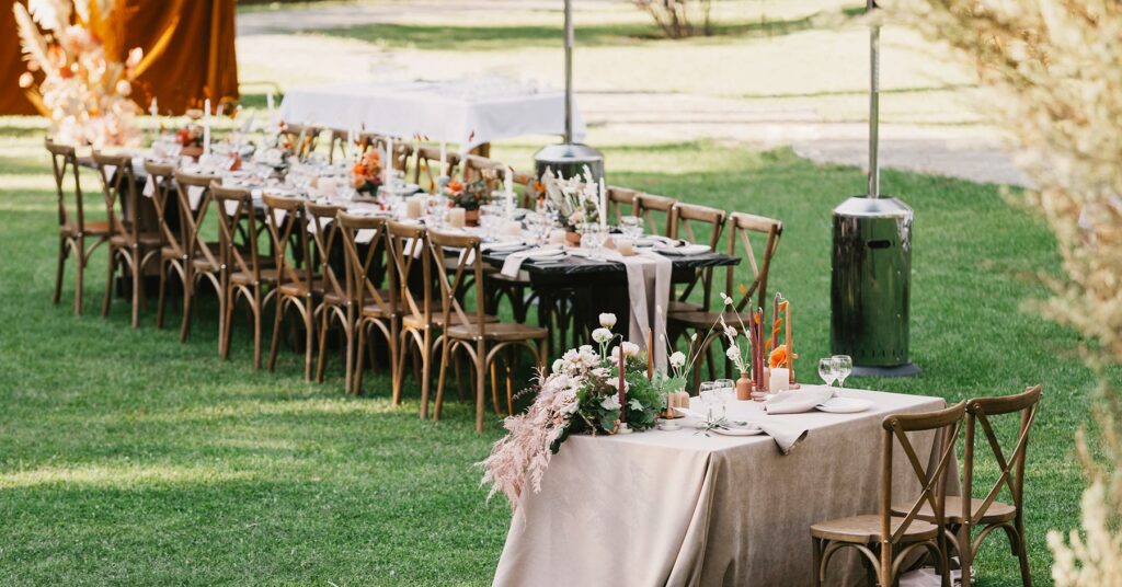 A long table and chairs with centerpieces and a sweethearts table is set up at a small backyard wedding reception