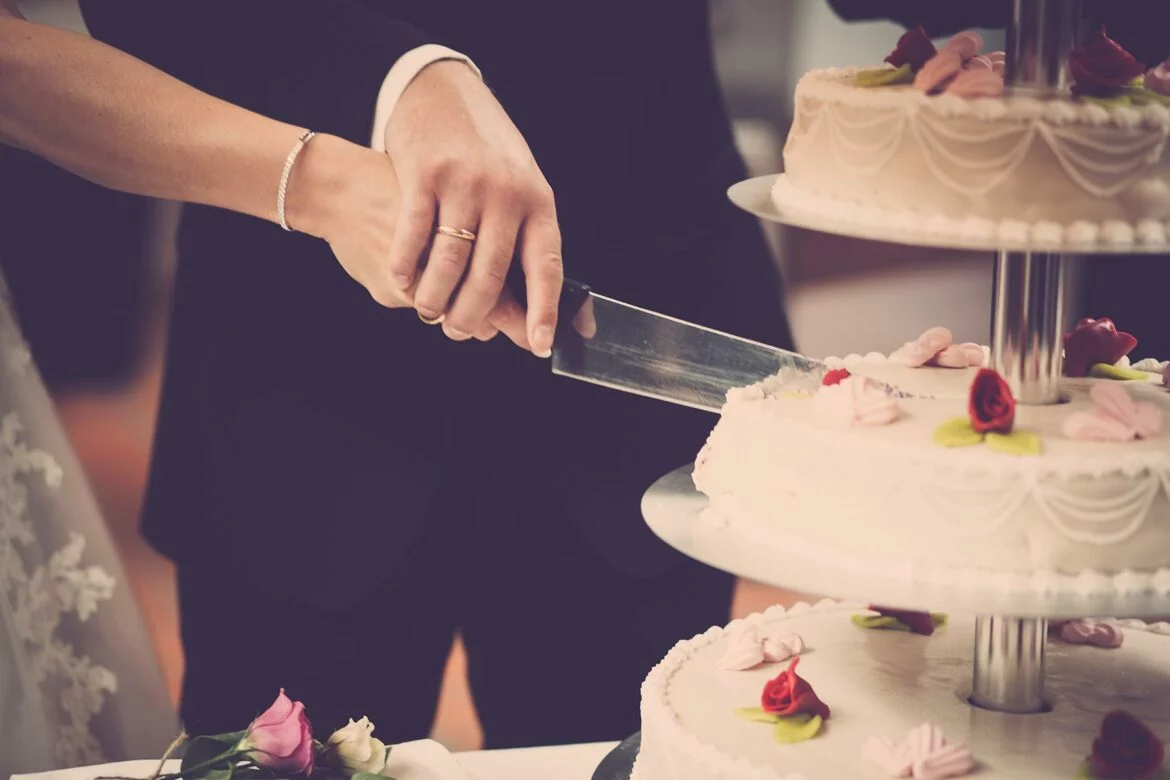 A close-up of two hands holding a knife and cutting a wedding cake