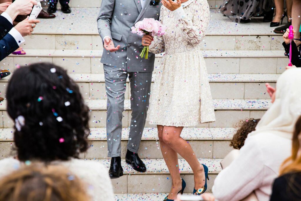 A couple wearing a short dress and suit after their wedding on the steps of a venue
