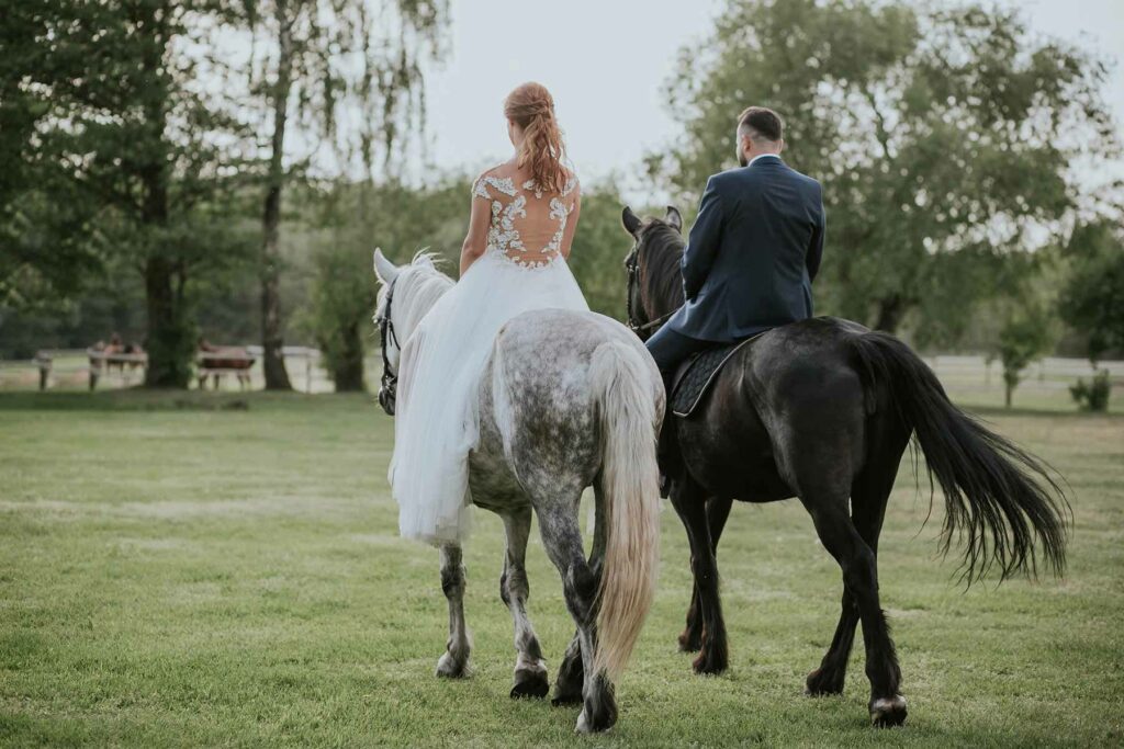 A couple in wedding attire riding horseback on a grassy field