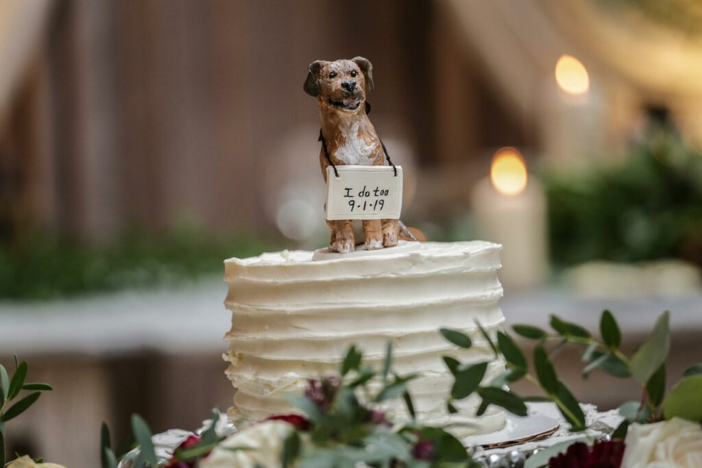 A wedding cake topper featuring a dog wearing a sign with the wedding date