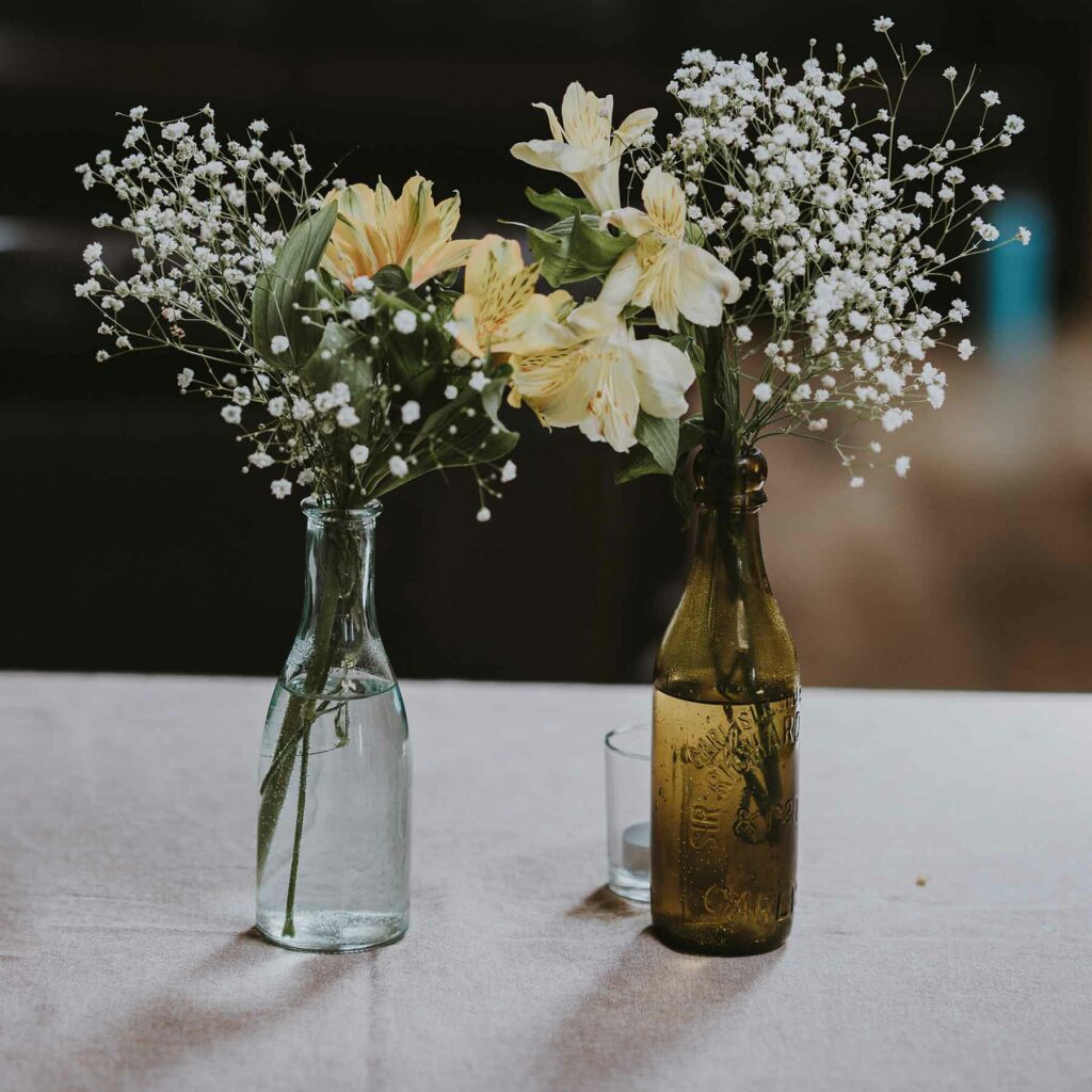 Bottles as bud vases create a refined wedding centerpiece with cream flowers and baby's breath