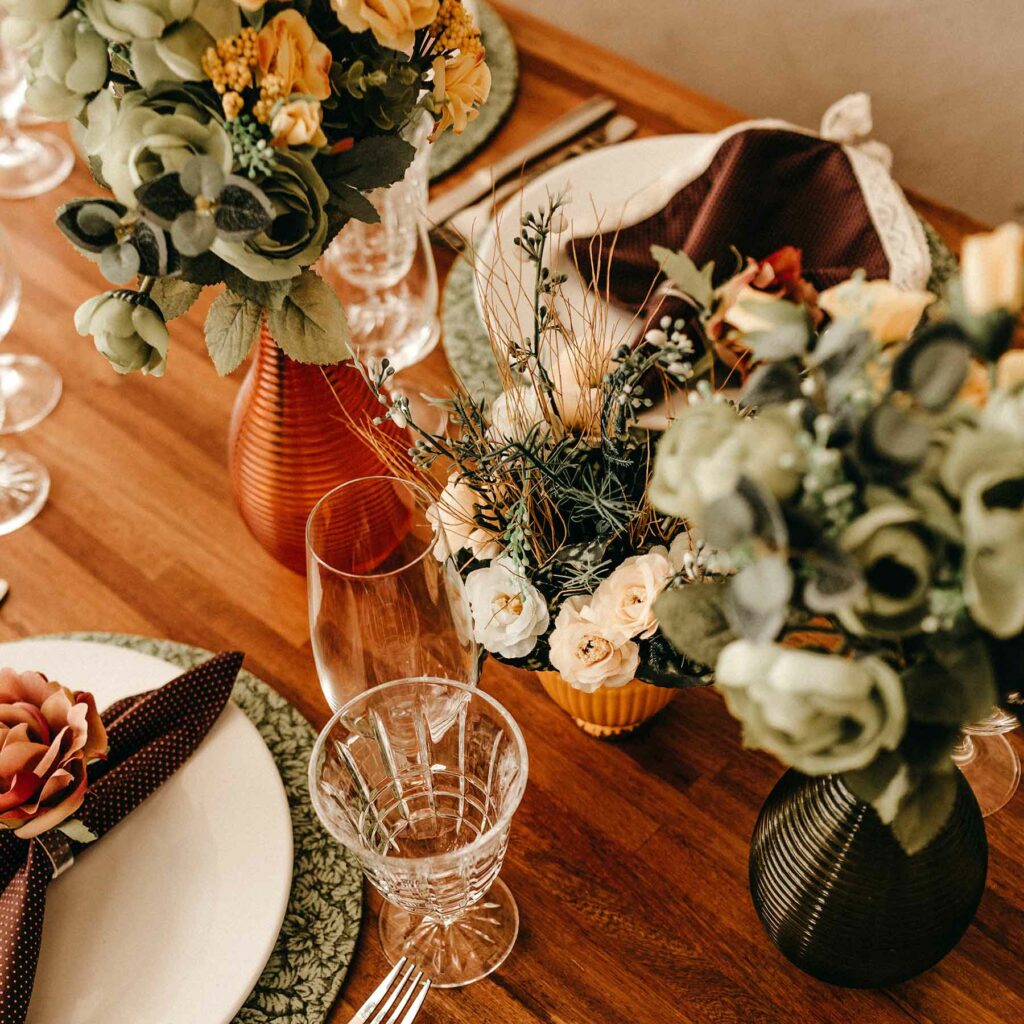 Rustic table holds floral bouquets in orange, black, and golden colored vases