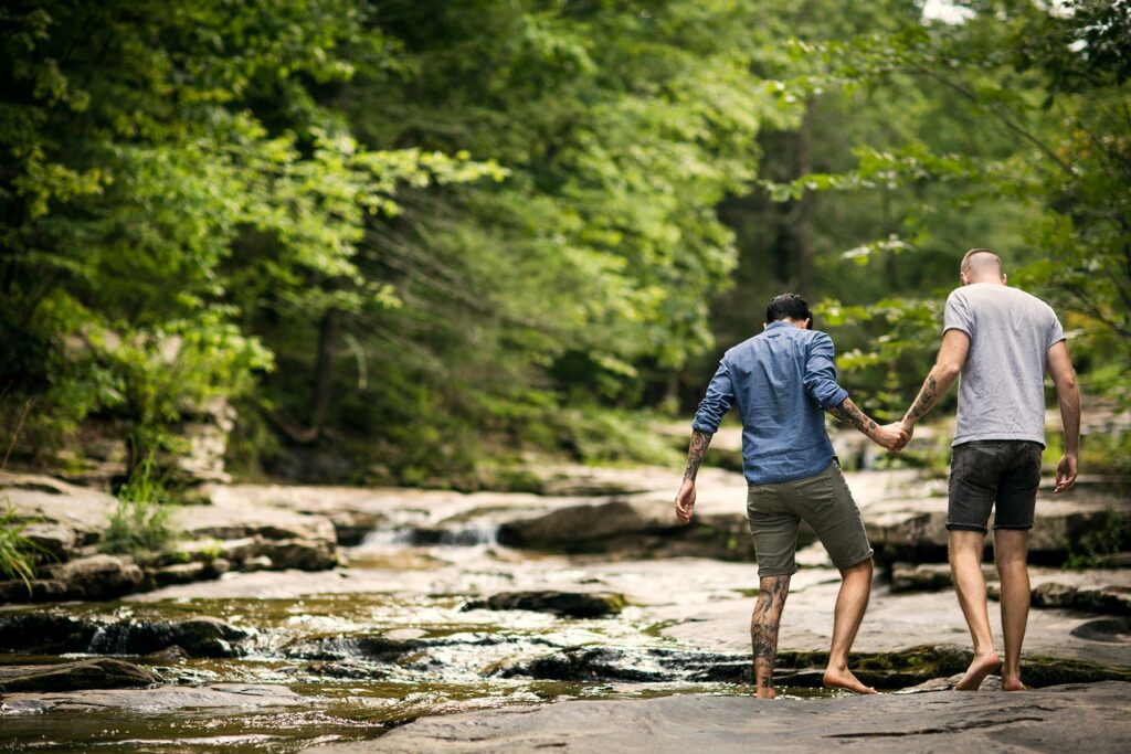 A couple holding hands while crossing a stream surrounded by trees