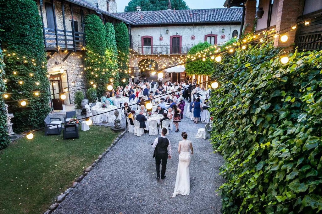 A couple walking into their outdoor wedding reception venue that is lit up with strands of twinkle lights