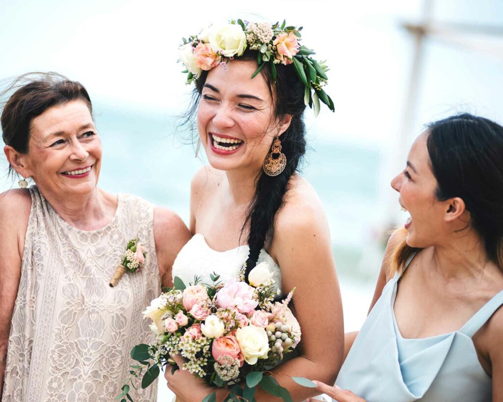 A bride wearing a flower crown with her mother and a wedding party attendant
