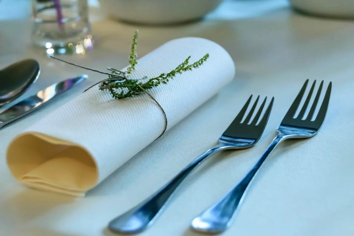 Stainless steel forks, knife, and spoon at place setting accompanied by cups and napkin