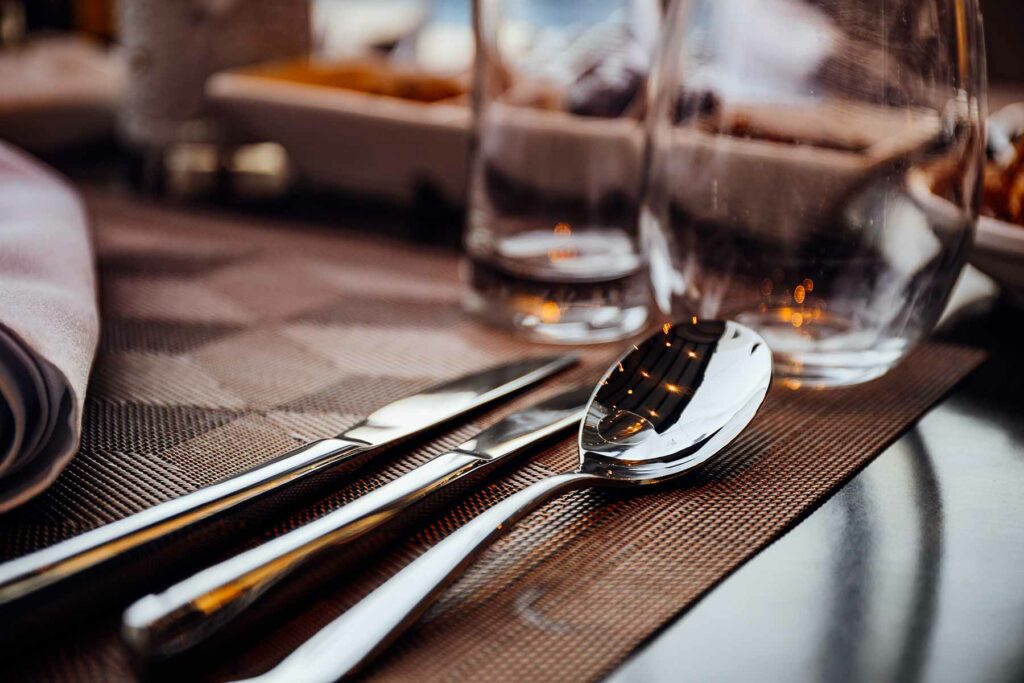 Place setting with fork, knife, plate, coffee cup, saucer, and water glass is on a white table