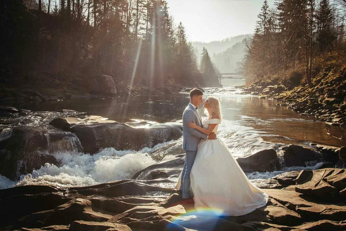 A couple holding hands while standing on river rocks after their destination wedding