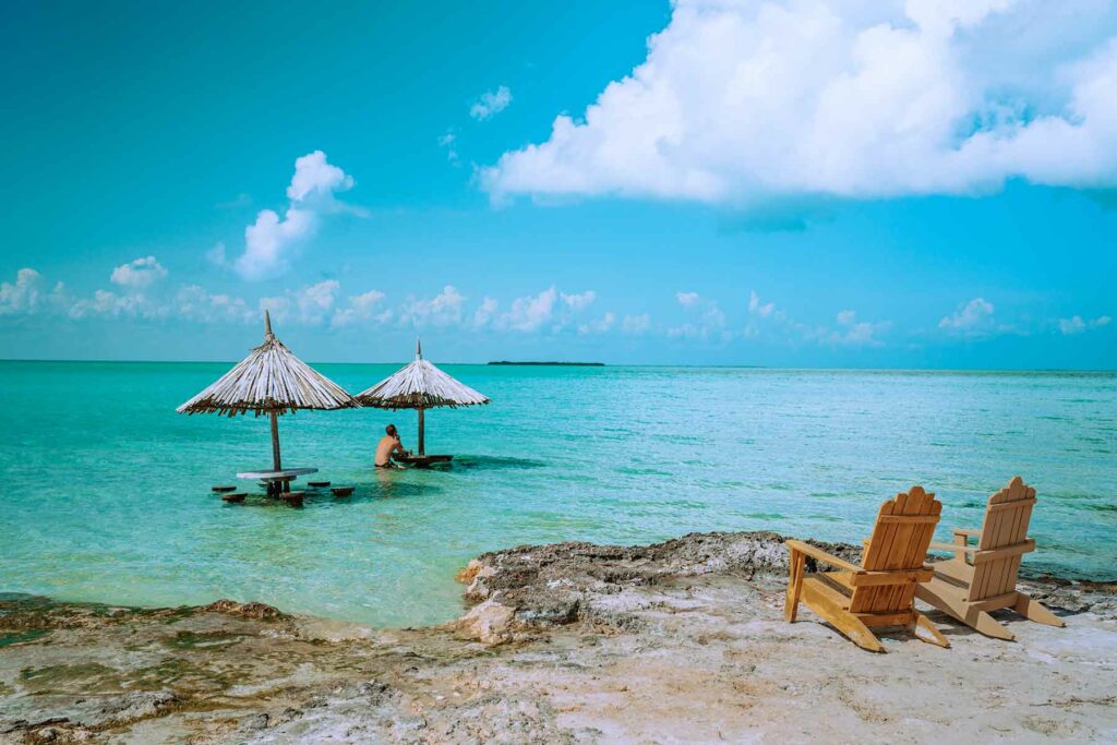 A man sitting under a thatched umbrella in the water at Secret Beach in Belize