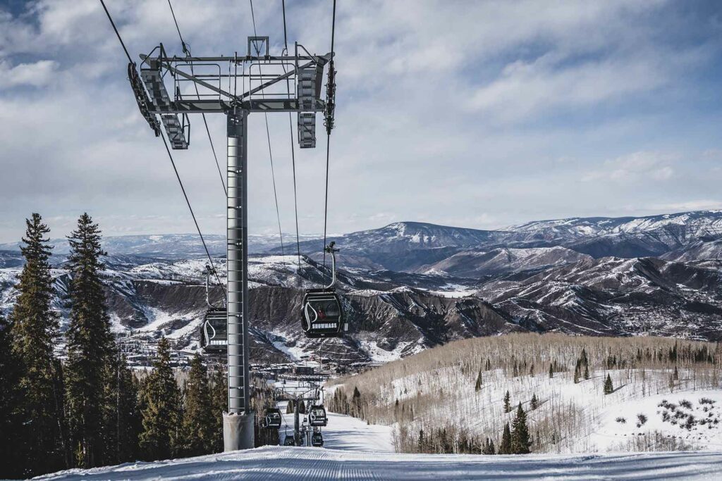 A ski lift with snow on the ground and snowcapped mountains in the background in Colorado honeymoon destination Aspen