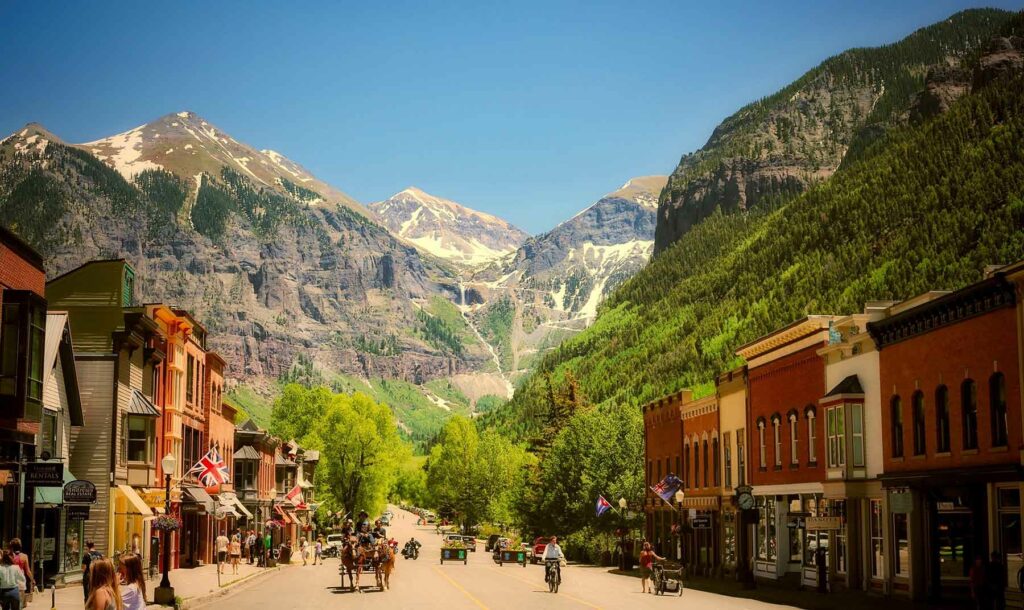 A small town street flanked by buildings and green trees with mountains in the background Colorado honeymoon destination Telluride