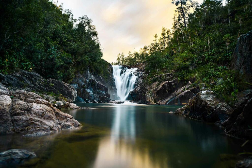 A view of a waterfall at Big Rock Falls in Belize surrounded by tall trees and rocks