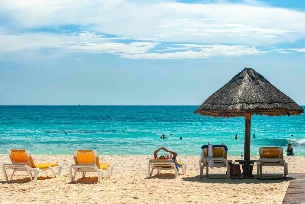 Lounge chairs and a thatched umbrella looking out at turquoise waters in Cancun, Mexico 