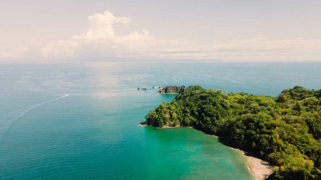 a point of land in Costa Rica covered in a canopy of trees, surrounded by water