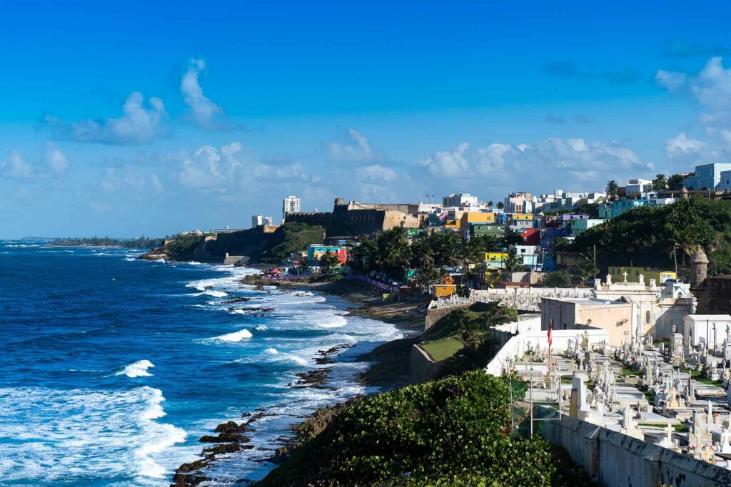 Waves crashing against the coastline and tree-lined cliffs with colorful buildings in San Juan, Puerto Rico