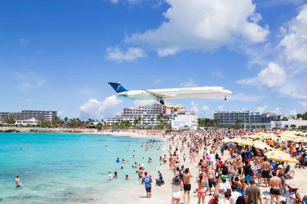 A plane flying low over a busy Maho Beach in St. Maarten