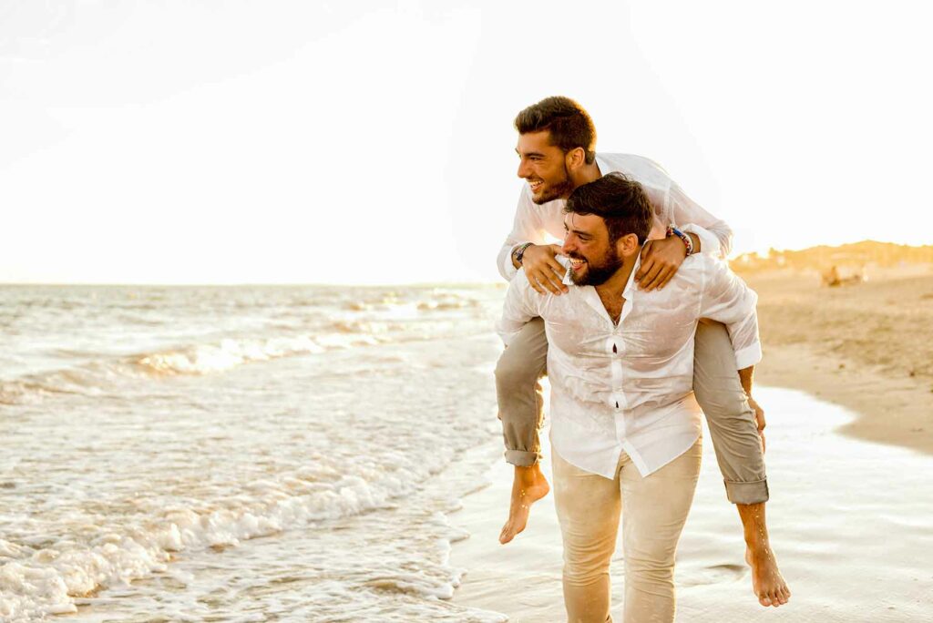 A man carrying his partner on his back during their beach honeymoon  walking along the shore