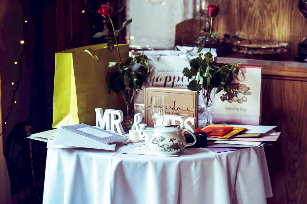 Round table decorated with “Mr & Mrs” sign and filled with wedding gifts and envelopes