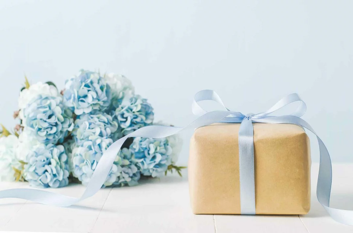 A wedding registry gift tied with a bow next to a bouquet of wedding flowers
