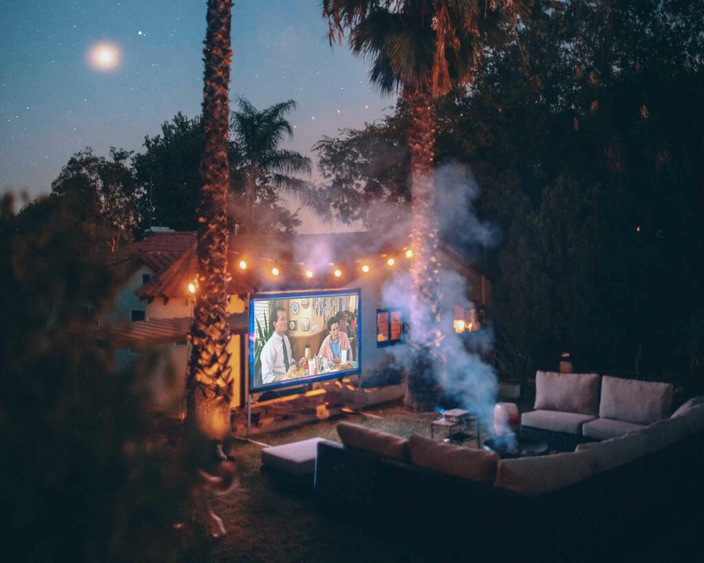 An outdoor proposal in a backyard during movie night with string lights above a screen between two palm trees 