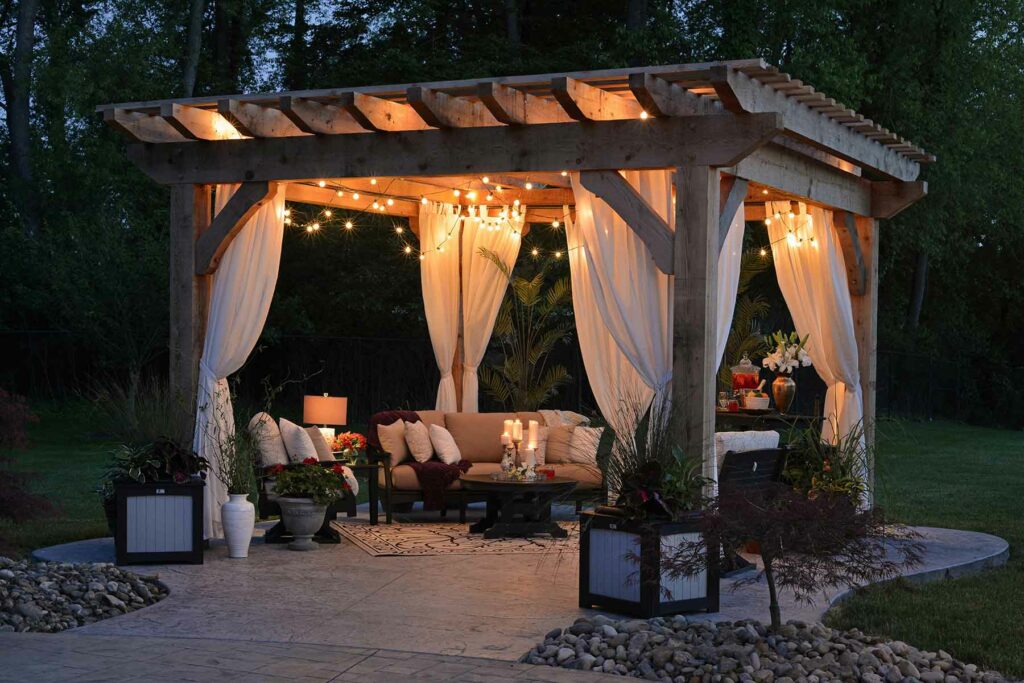 An outdoor proposal setup under a gazebo decorated with natural seating, string lights and flowers