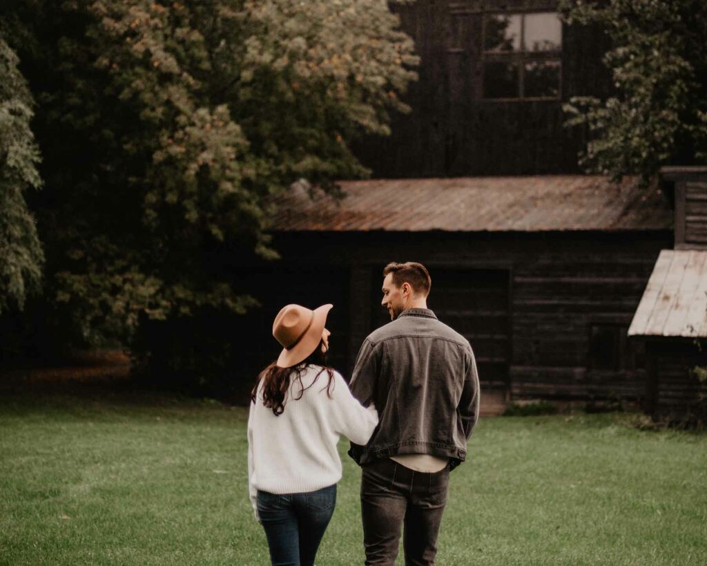 A couple on a farm during an outdoor proposal walking toward the barn