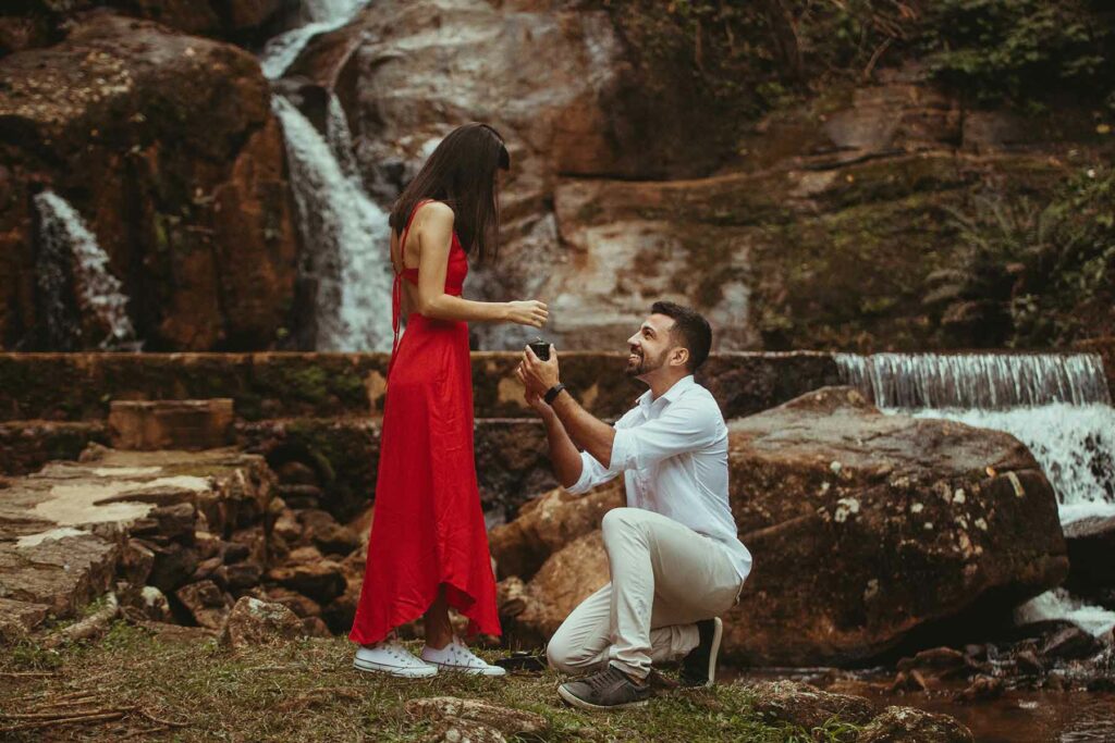 An outdoor proposal at the end of a hike with a man on bended knee holding a ring