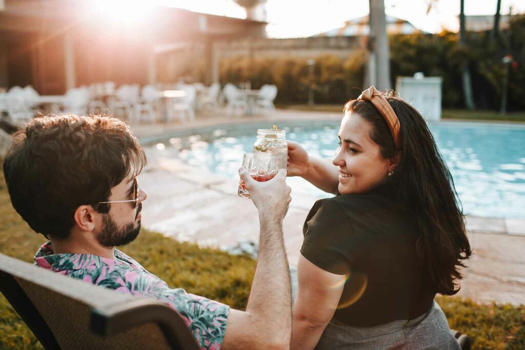 A couple clinking glasses during an outdoor proposal at a pool