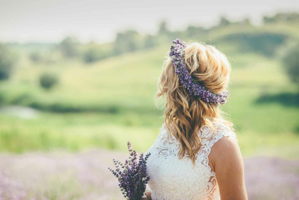 A woman wearing a wildflower flower crown and a wedding dress looking at green hills