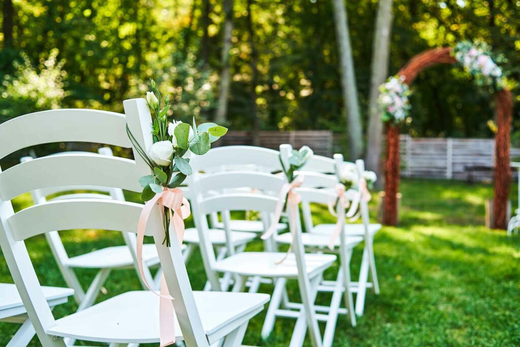 Spring wedding ceremony decor with chairs tied with ribbons and fresh flowers and an arch made out of branches