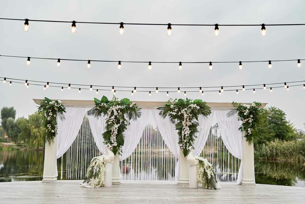 Reception decor with white linens, greenery and twinkle lights over a dance floor
