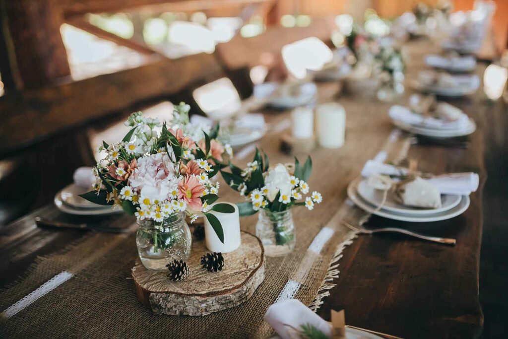 Rustic themed spring wedding table with a burlap table runner and spring blooms in mason jars