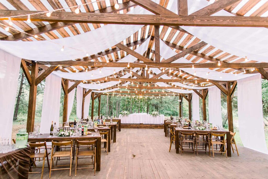 Rustic tent draped in light fabric and twinkle lights with tables set up for a spring wedding