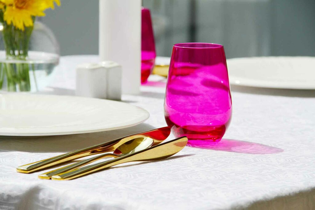 Bright stemless wine glass sits next to plate and flatware on white tablecloth