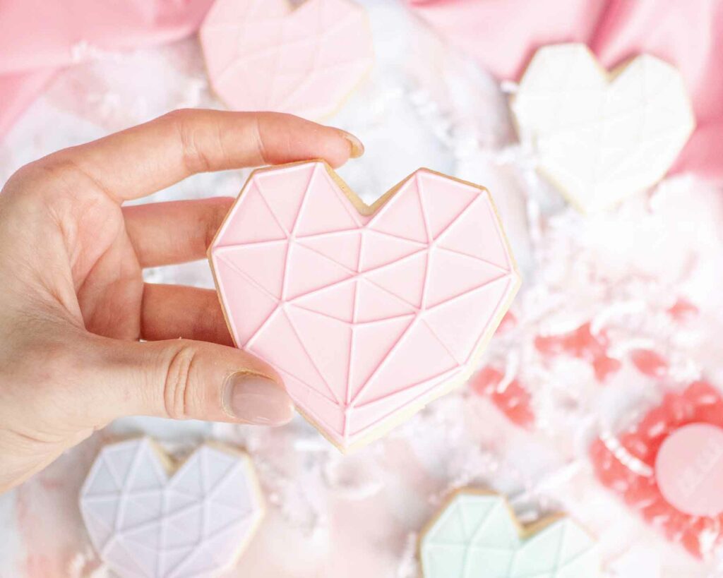 Person holding heart-shaped, decorated sugar cookie