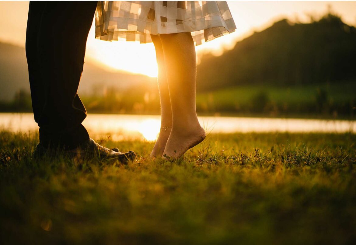 Close-up of a man and woman's feet standing on grass during golden hour