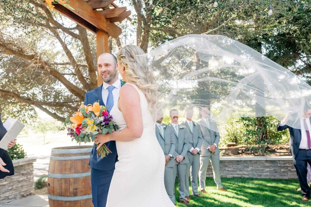 A couple getting married at the Fairview Napa in front of an aged wine barrel with the wedding party looking at them