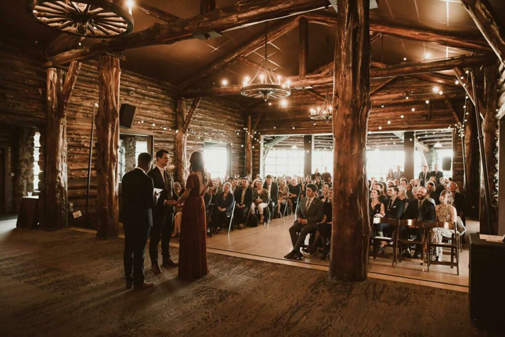 A wedding ceremony taking place inside the Log Cabin at the Presidio wedding venue, a rustic looking building with wagon wheel chandeliers