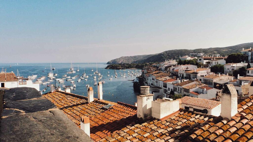 A view of the Costa Brava coastline with boats and the water surrounded by red-roofed white buildings