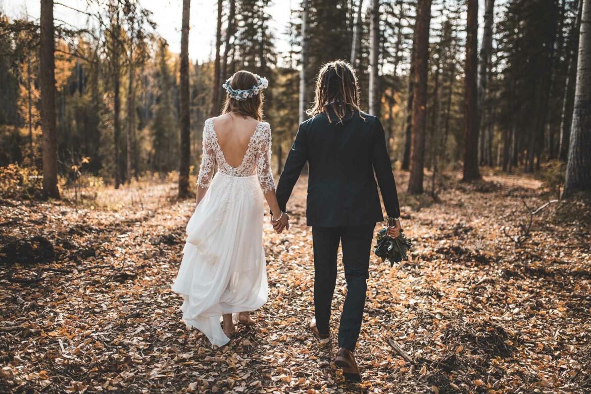 A couple walking through the woods hand in hand at their fall wedding wearing a flower crown and wedding dress and a suit