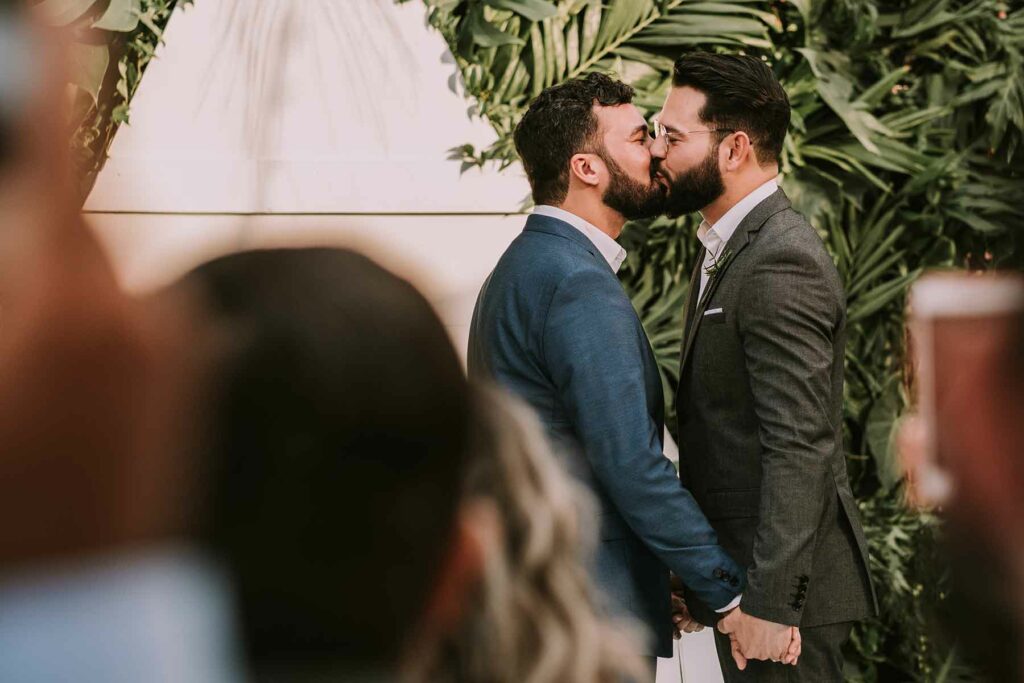 Couple kissing at a fall wedding while wearing suits in forest green and navy