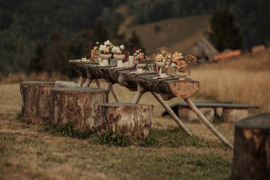 Rustic fall wedding table made of a log supported by wooden legs and tree stumps as chairs