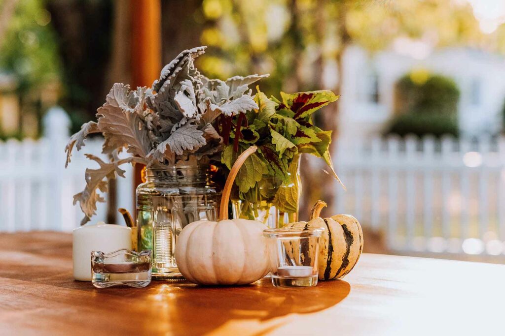 A fall wedding centerpiece idea with candles, mini gourds and mason jars holding greenery
